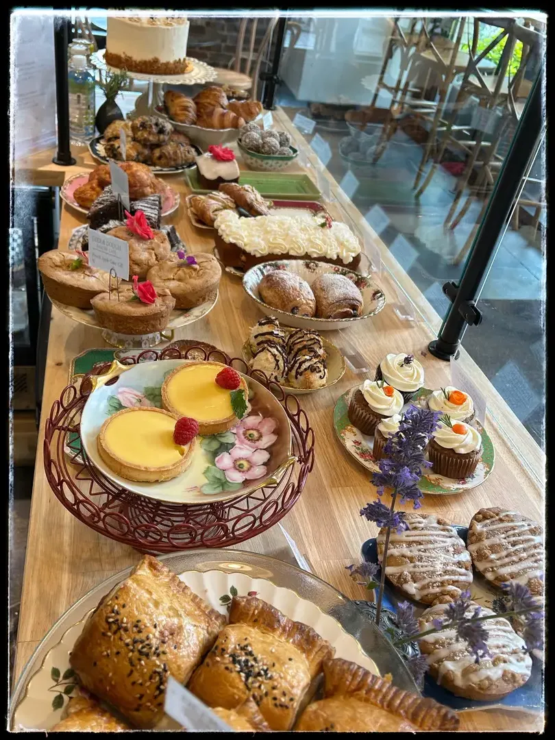 Bakery counter with assorted pastries including croissants, cakes, and tarts, with a menu board in the background.