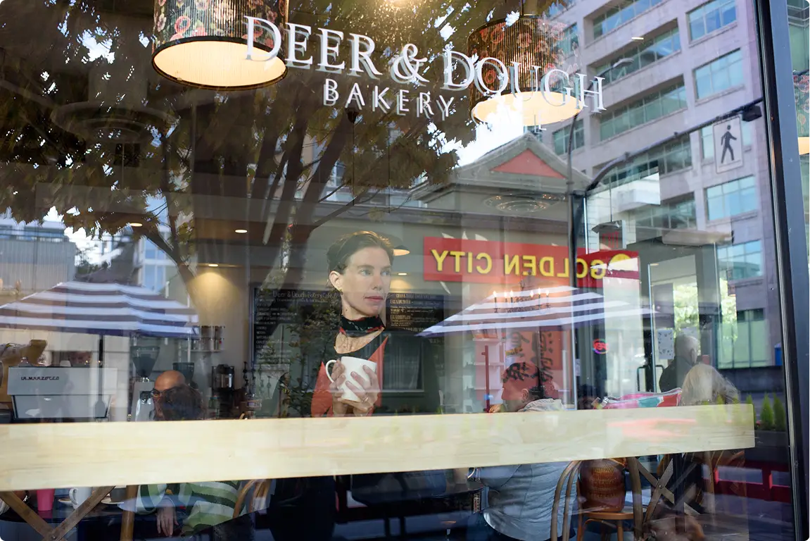 View through Deer & Dough Bakery window showing people inside and street reflections.