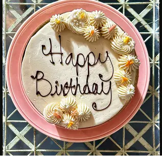 Round birthday cake with floral decorations and 'Happy Birthday' written in chocolate on a pink plate.