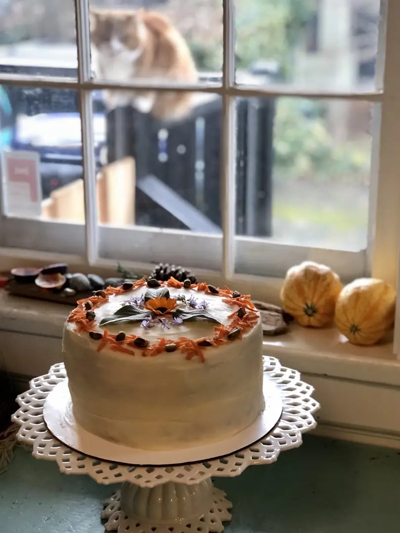 Decorated cake on a stand with a cat outside.