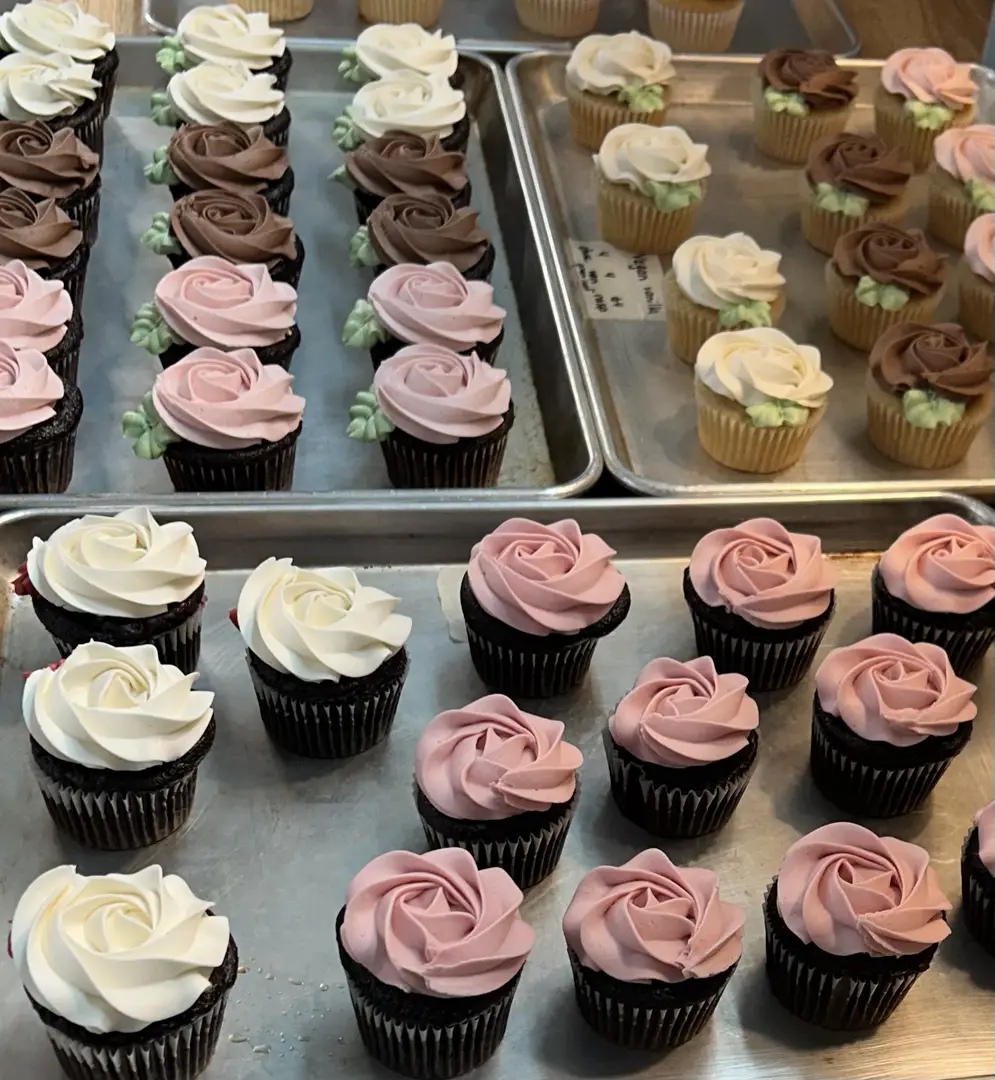 Rose frosted cupcakes on trays.